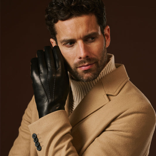 Man wearing a beige coat and black leather gloves against a brown background
