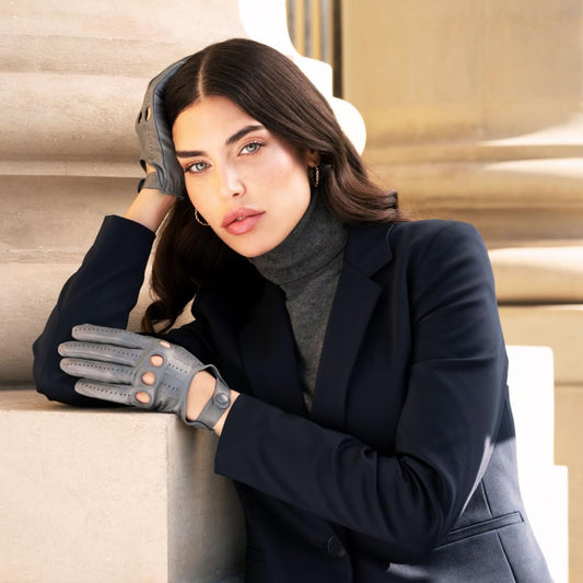 Woman wearing a dark coat and gloves leaning against a wall.