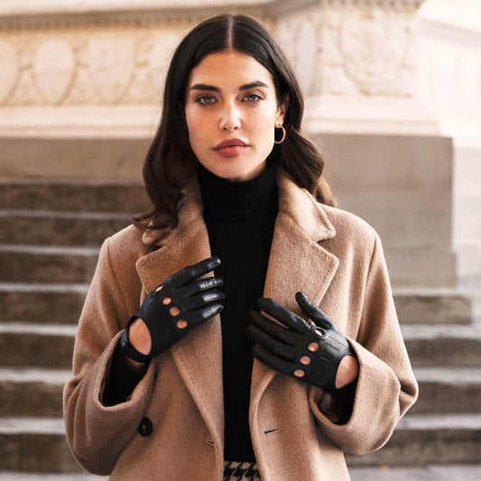 Woman wearing a beige coat and black gloves standing on steps.