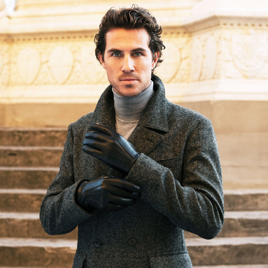 Man wearing a gray coat and black gloves standing on steps with classical architecture in the background