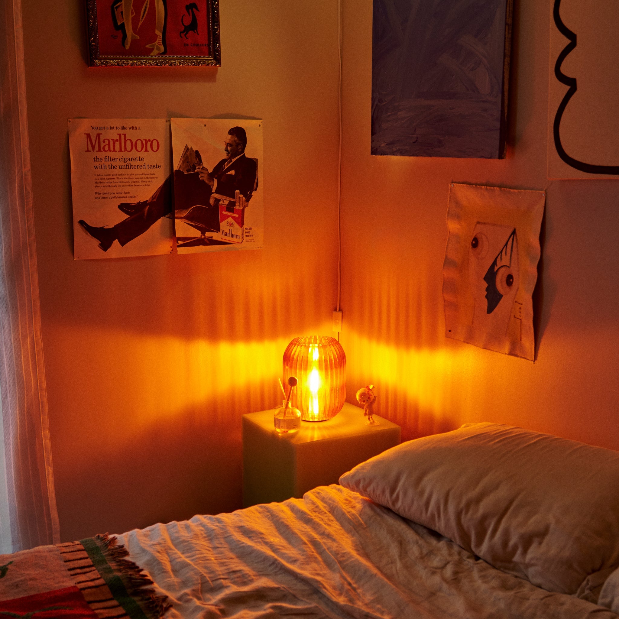 Bedroom with warm lighting, Marlboro advertisement on wall, and lit lamp.