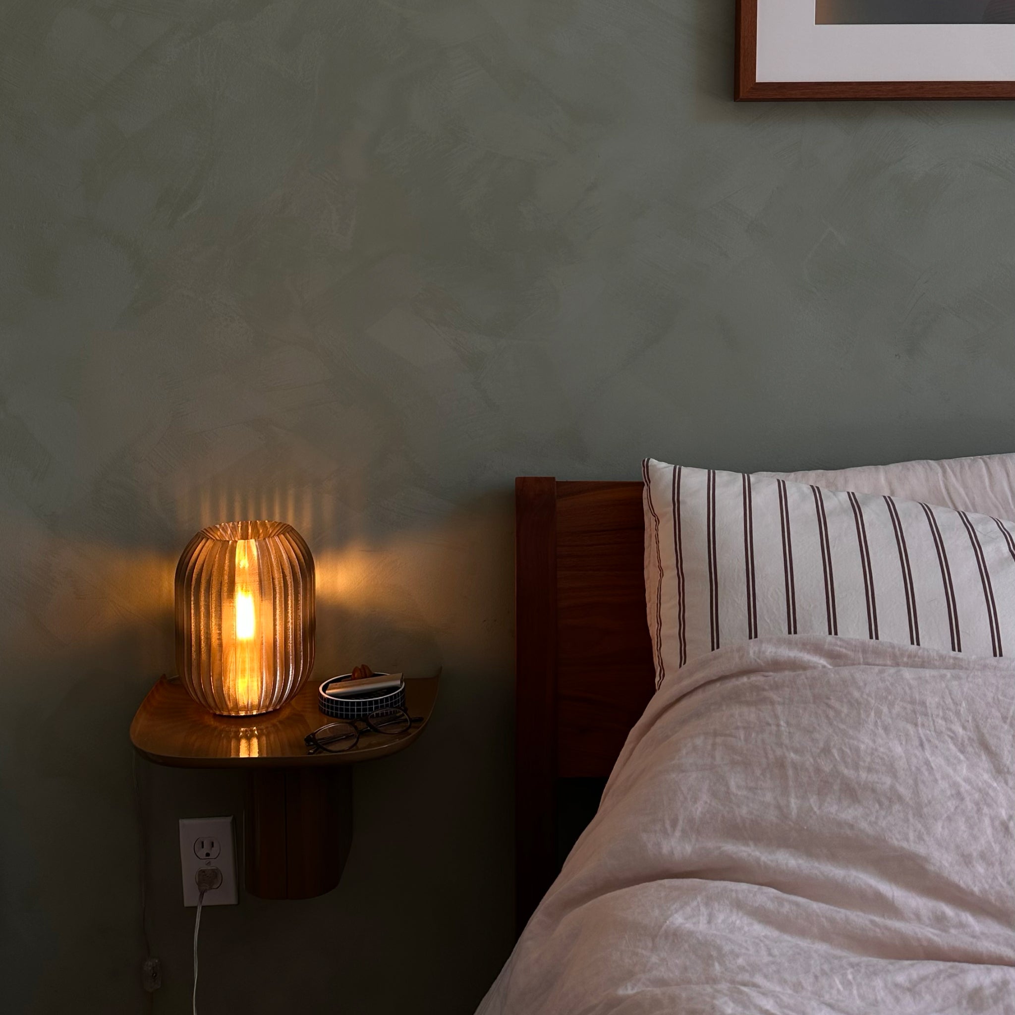 Bedroom with a nightstand featuring a lit lamp and a bed with striped pillows.