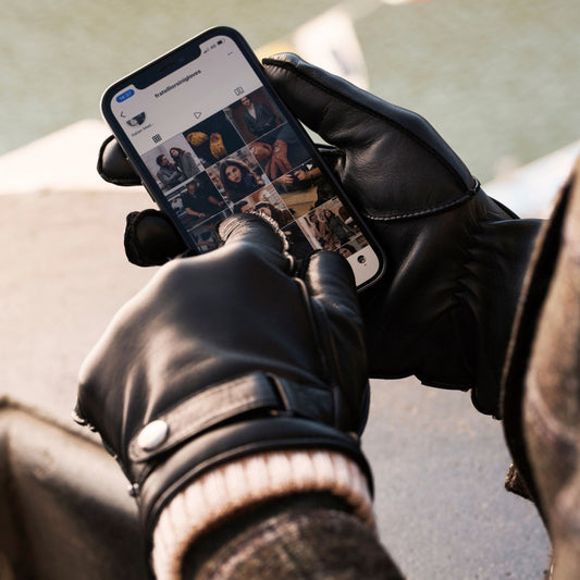 Person wearing black gloves using a smartphone with a blurred background