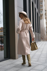 Woman in a long coat and hat walking on a city sidewalk.