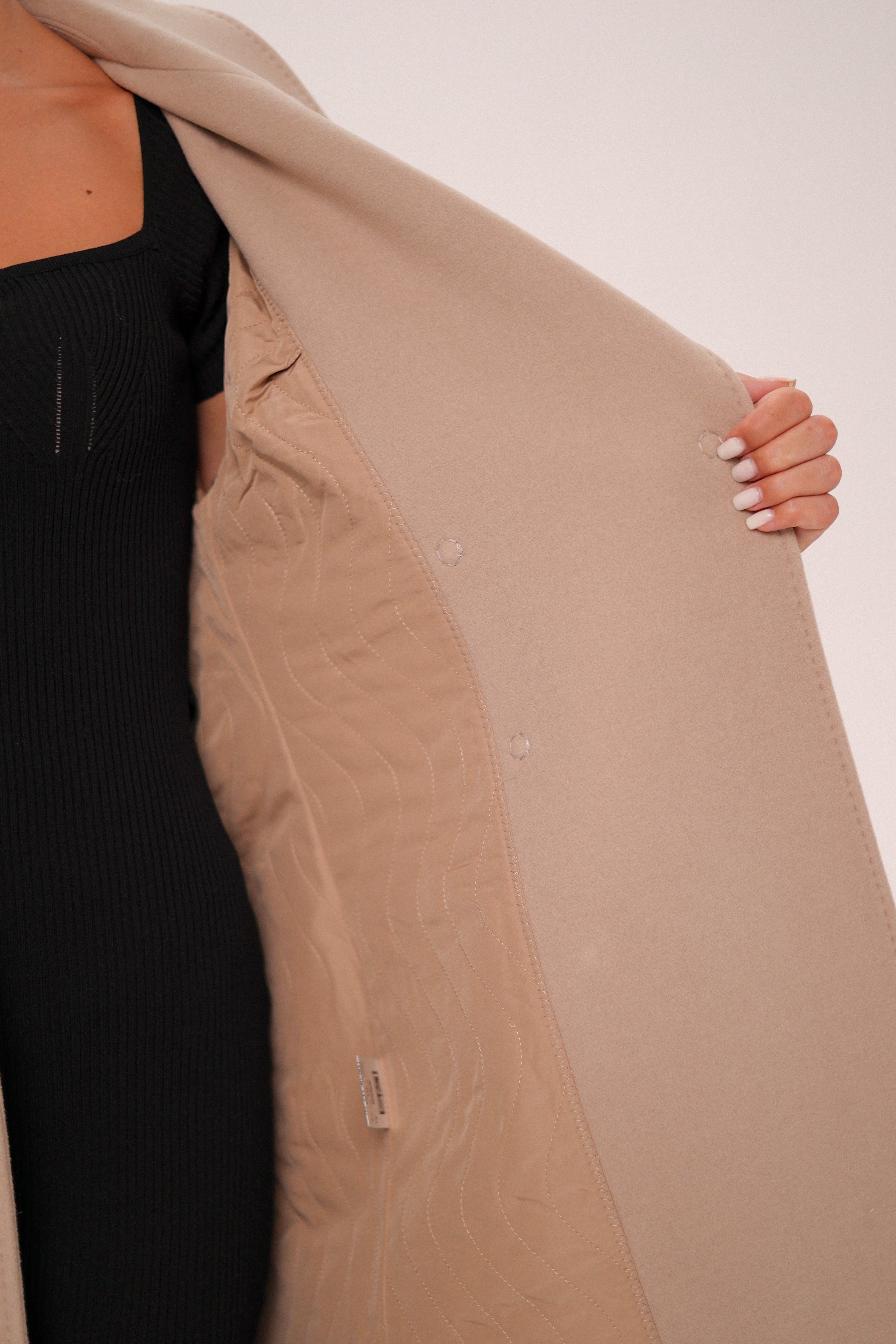 Person wearing a beige trench coat with a plain background