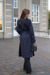 Woman in a long dark coat walking on a paved walkway with a building in the background.