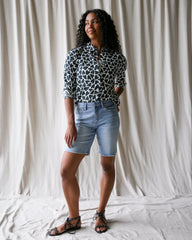 Woman wearing a patterned shirt and denim shorts standing against a plain background