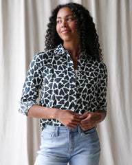 Woman wearing a patterned shirt and jeans against a white curtain background