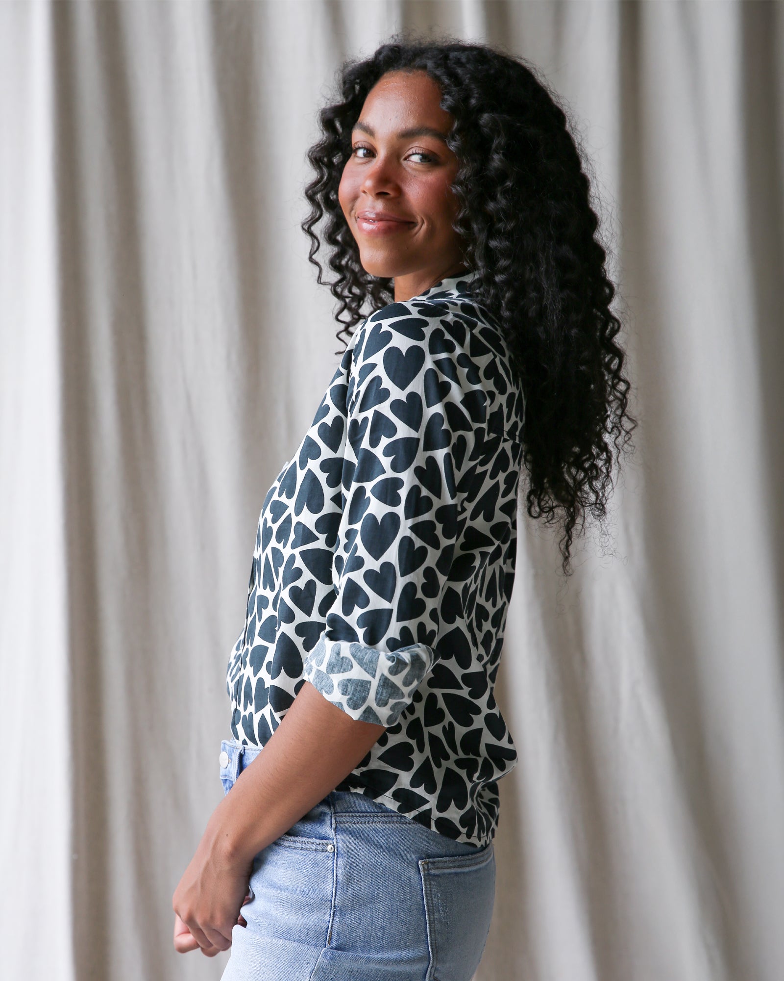 Woman wearing a patterned blouse and jeans against a neutral background