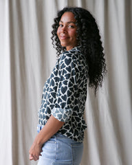 Woman wearing a patterned blouse and jeans against a neutral background