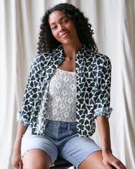 Woman wearing a patterned shirt over a lace top and denim shorts against a neutral background