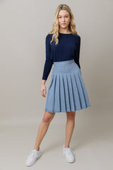 Woman wearing a navy sweater and light blue pleated skirt on a beige background