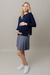 Pregnant woman wearing a navy top and gray pleated skirt on a beige background