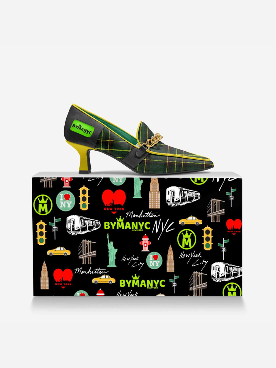 Green high-heeled shoe with yellow accents on a black shoe box featuring New York City icons.