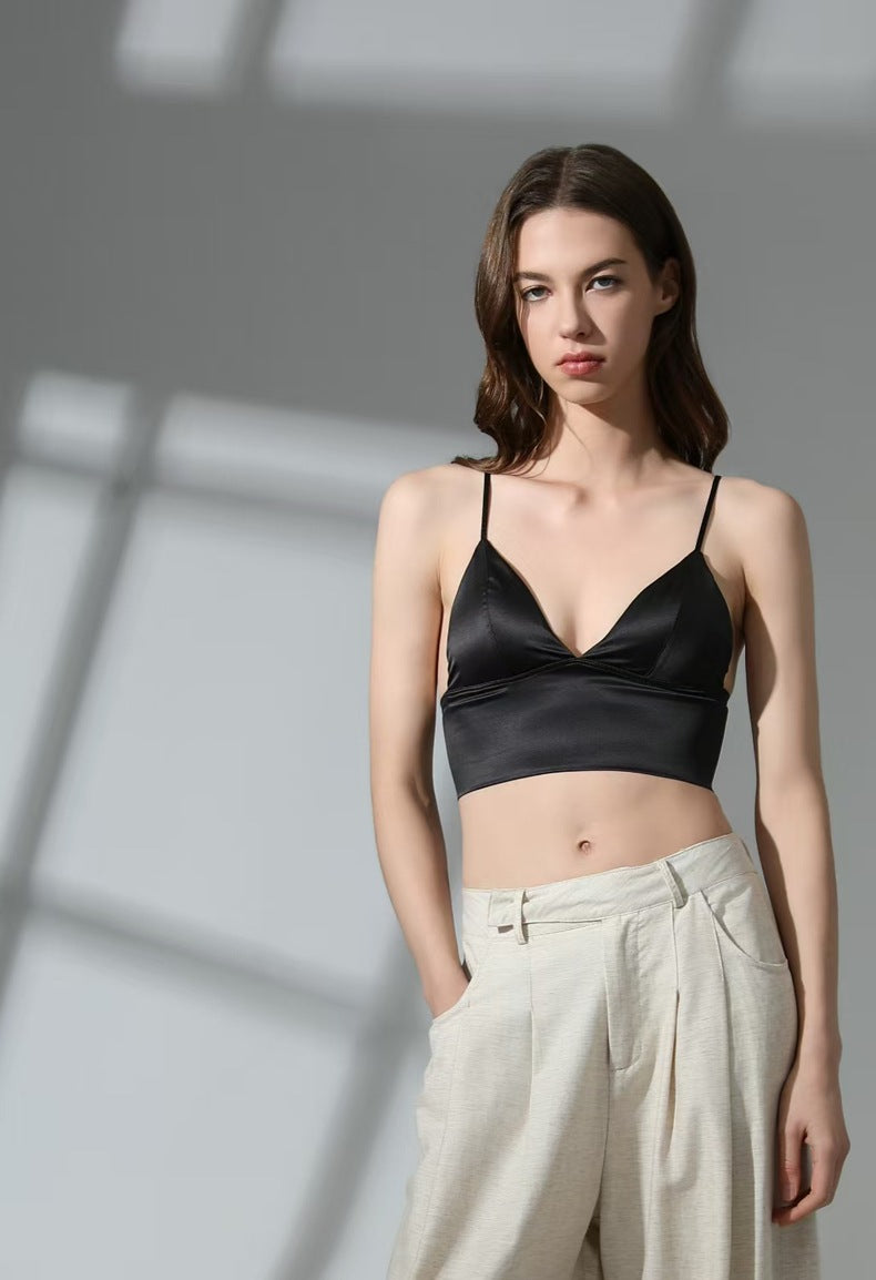 Woman wearing a black satin crop top and light-colored pants against a neutral background