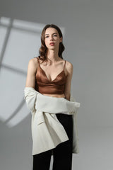 Woman wearing a brown top and white jacket against a gray background