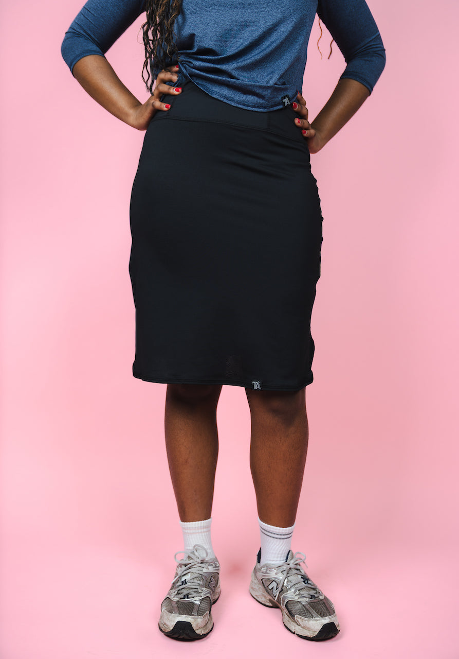Person wearing a blue top and black skirt on a pink background