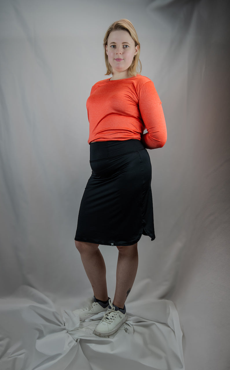 Person wearing an orange sweater and black skirt against a plain background