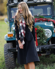 Woman wearing a black coat and plaid scarf standing in front of a teal SUV with Christmas decorations.