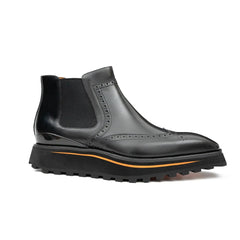 Black Chelsea boot with orange sole on a white background
