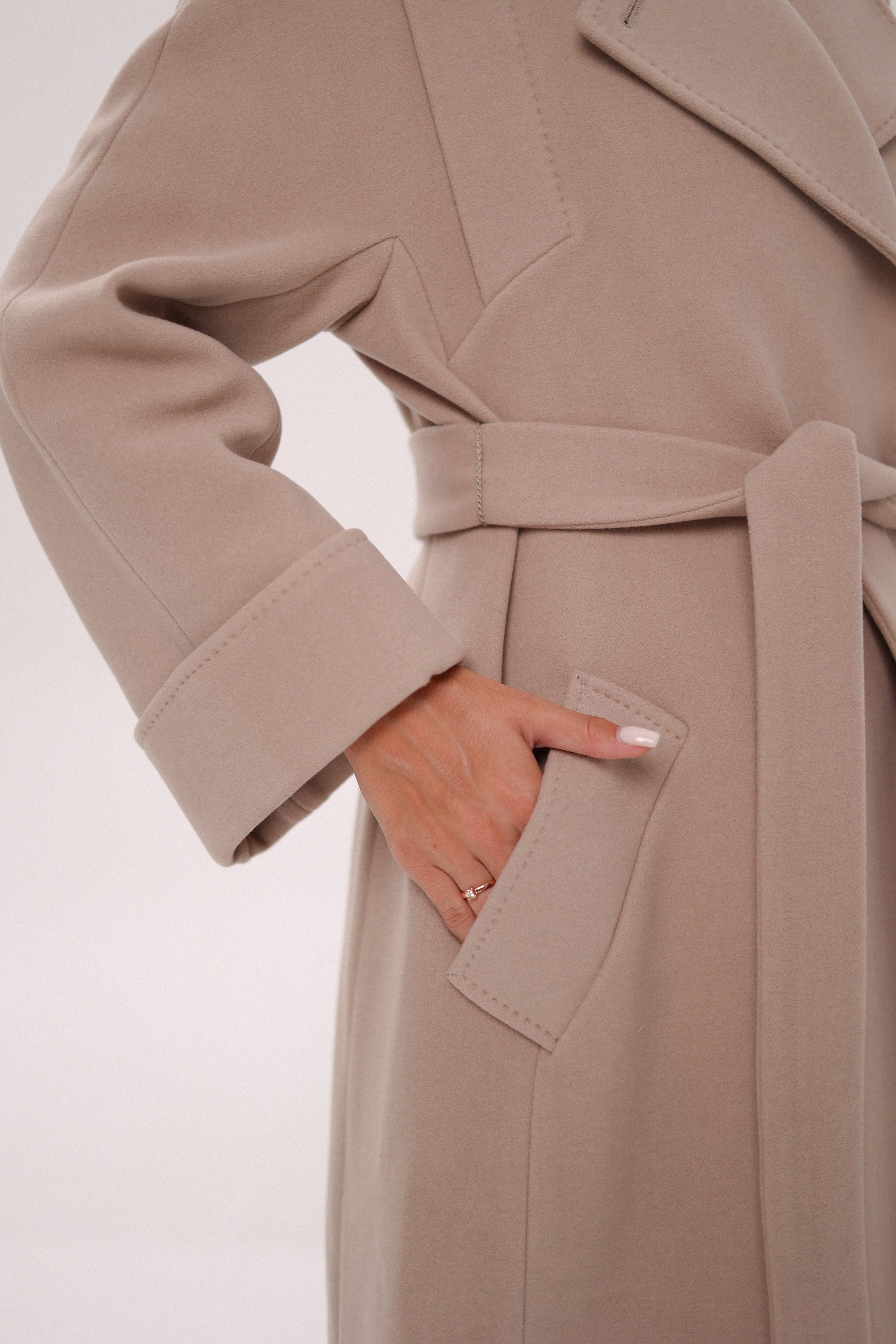 Close-up of a beige coat with a hand in the pocket on a white background