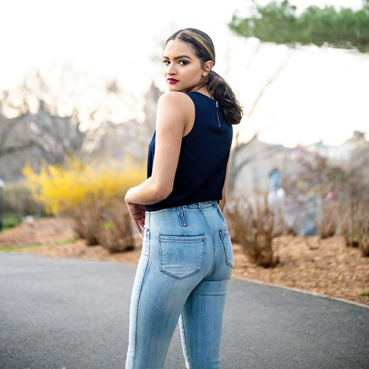 Woman wearing a navy sleeveless top and light blue jeans standing outdoors with blurred background