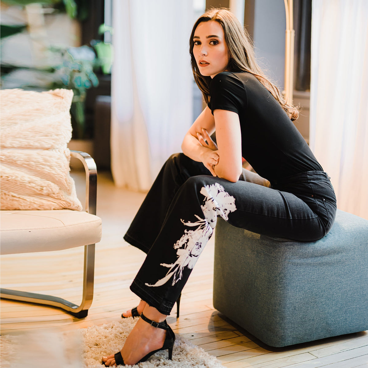 Woman sitting on a blue ottoman in a stylish living room.