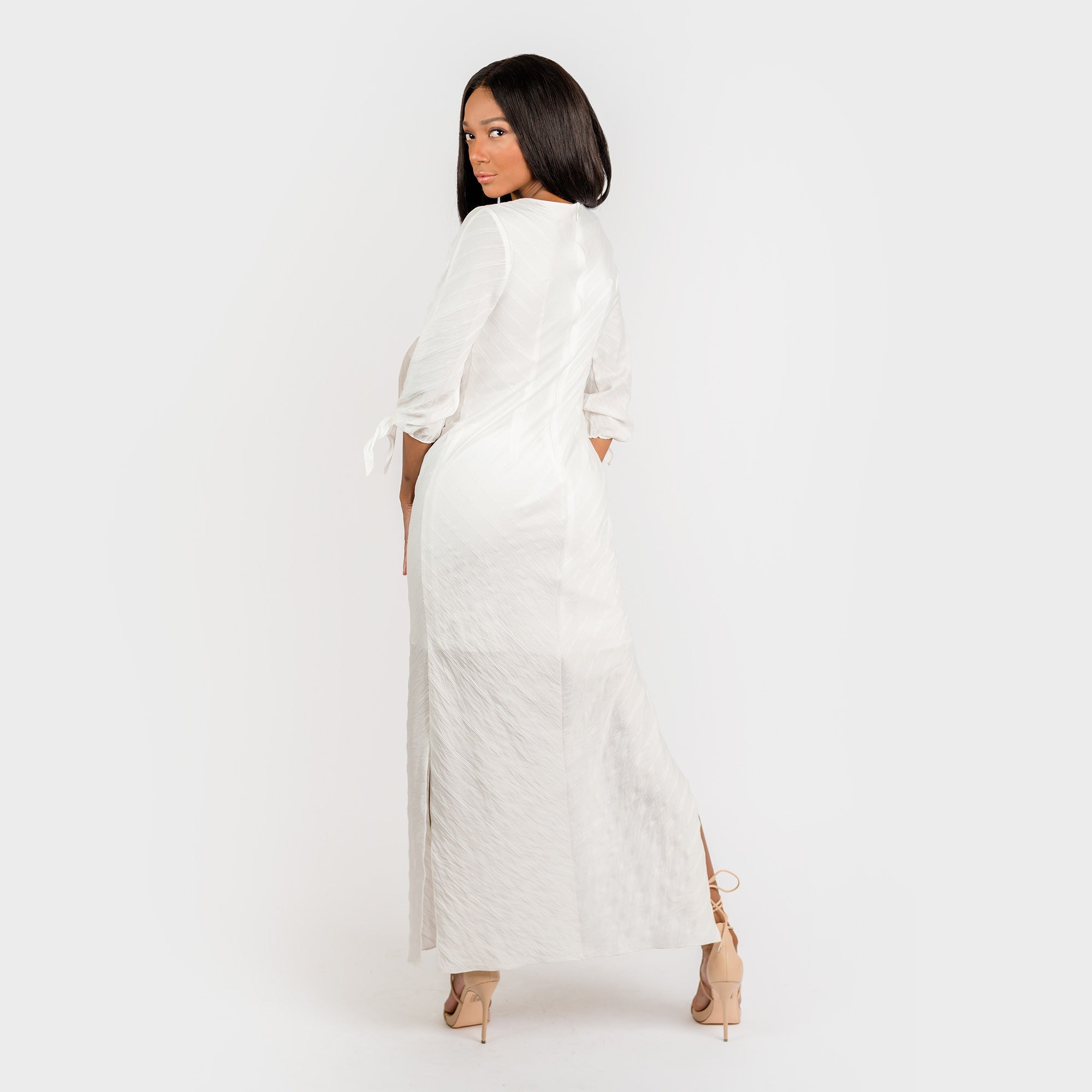 Woman wearing a white dress with long sleeves and a slit on a white background