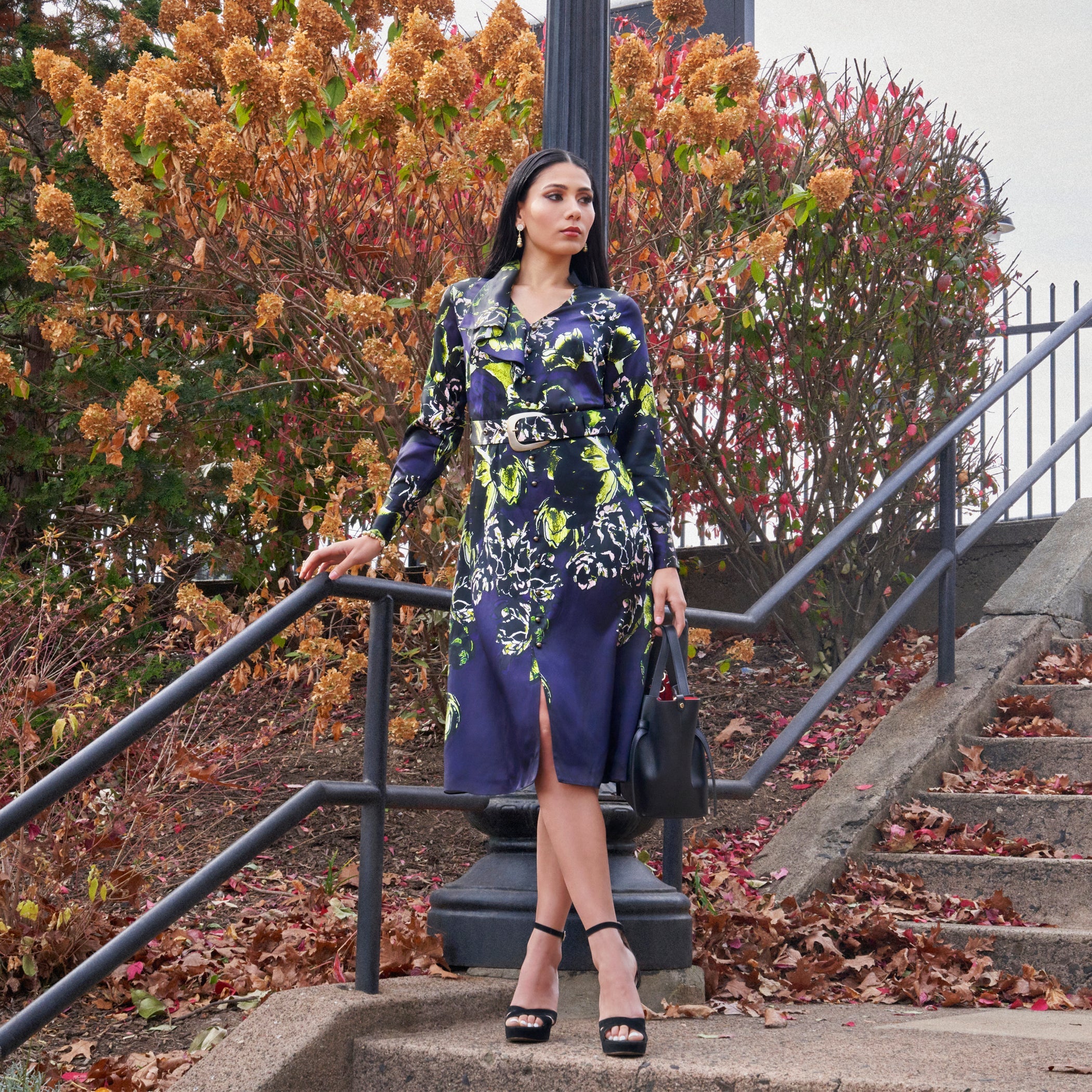 Woman in a floral dress standing on steps with autumn foliage in the background