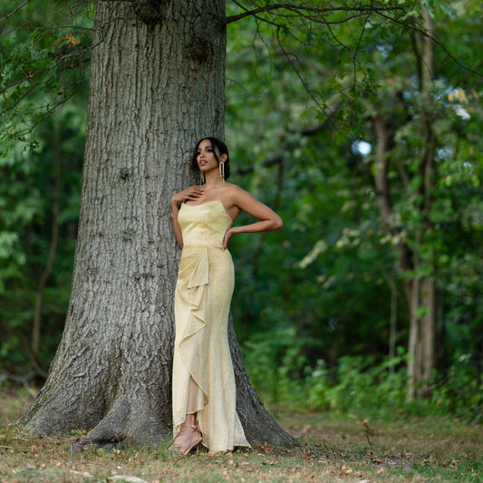 Woman in a yellow dress standing next to a tree in a forest