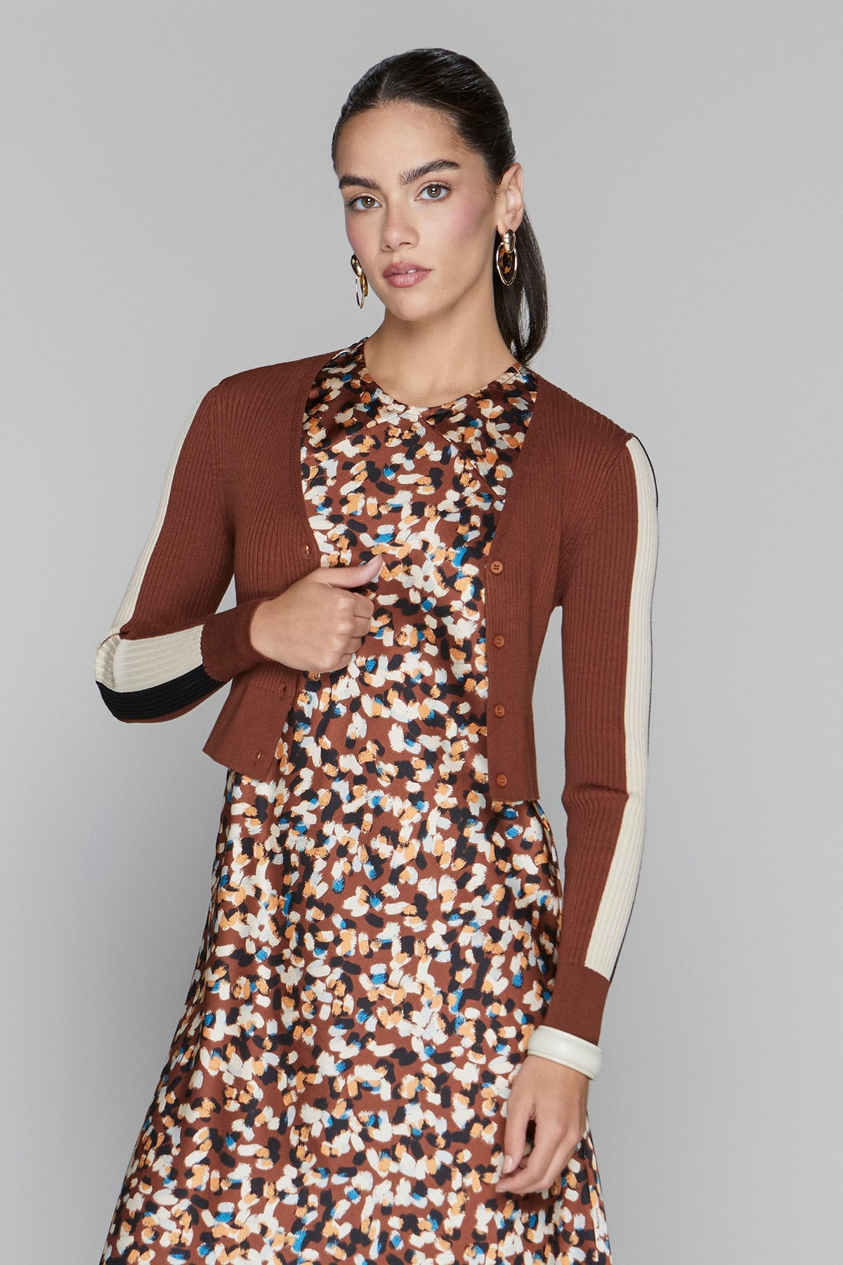 Woman wearing a brown blazer over a patterned dress on a gray background