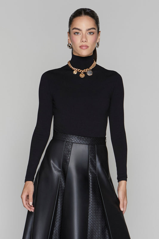 Woman wearing a black turtleneck and black leather skirt with gold jewelry on a gray background