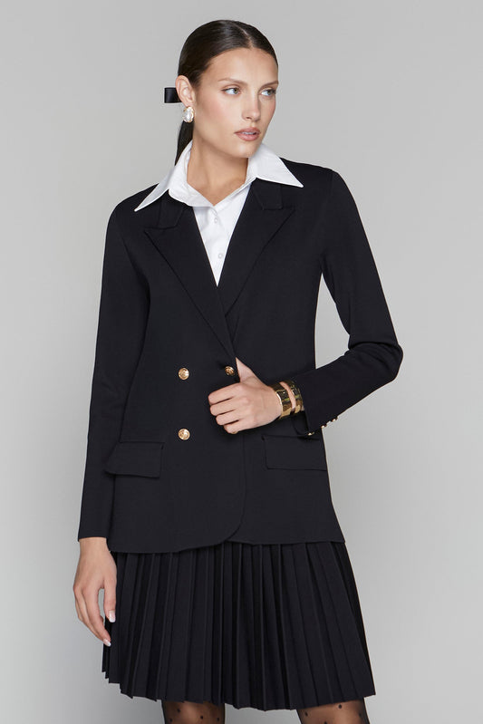Woman wearing a black blazer and black pleated skirt with a white shirt on a gray background