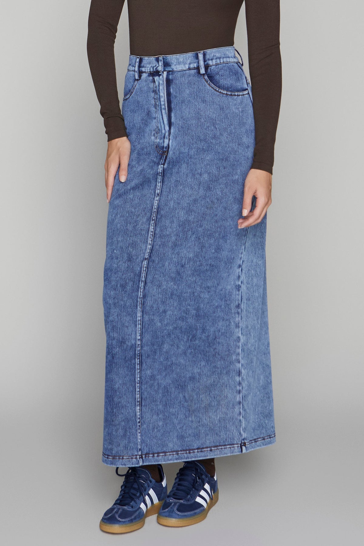 Person wearing a long blue denim skirt with a plain background