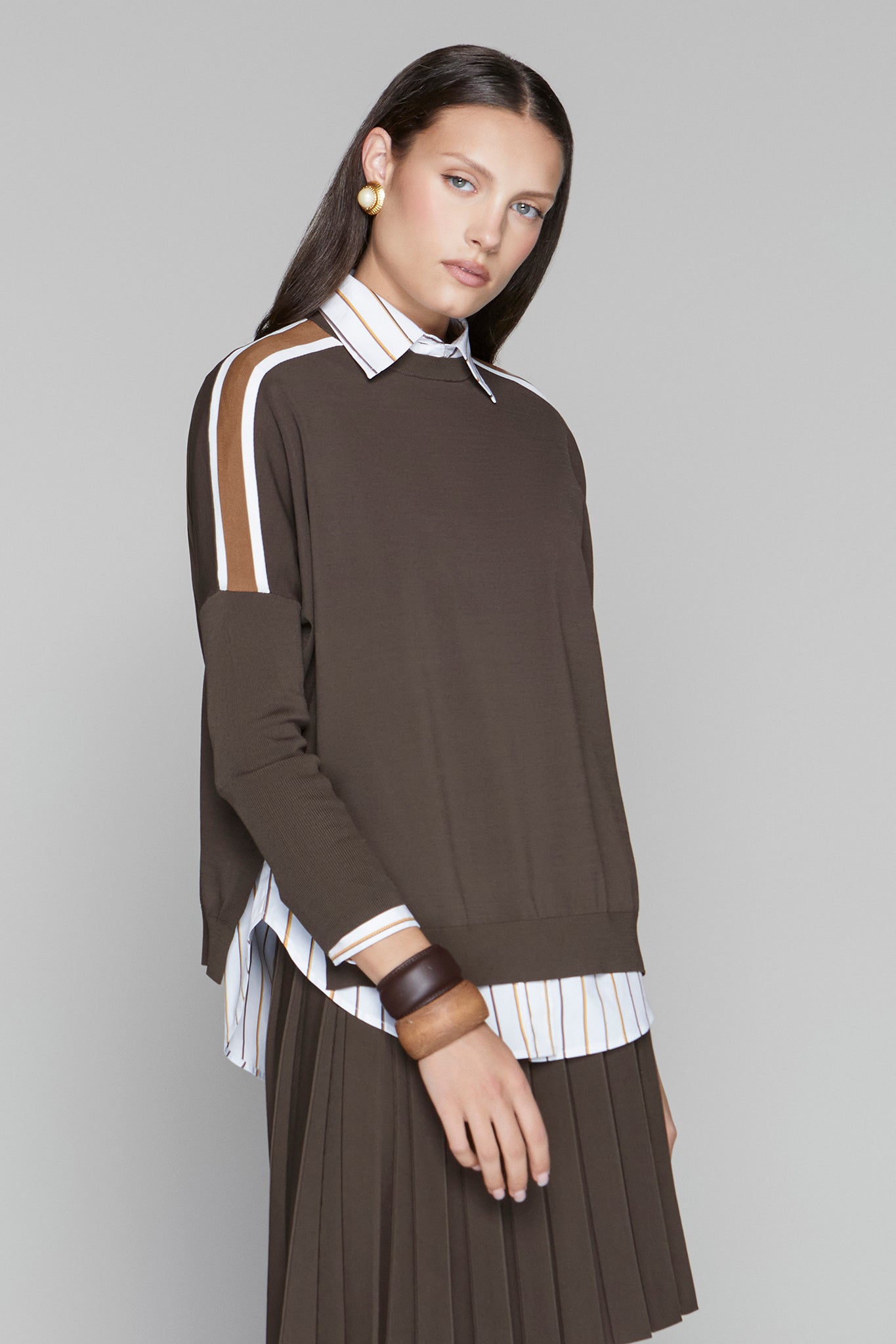 Woman wearing a brown dress with white and beige accents on a gray background