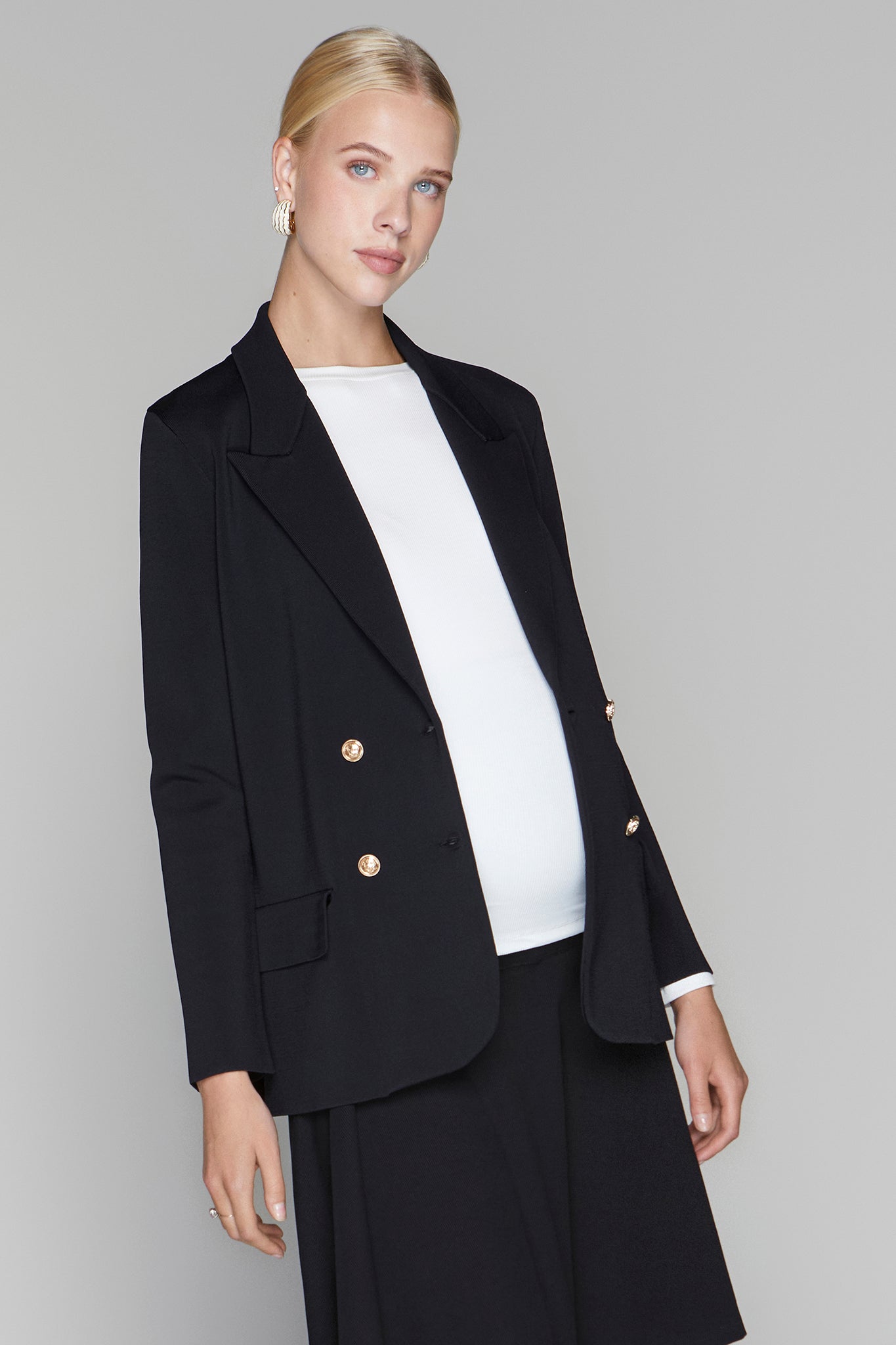 Woman wearing a black blazer with gold buttons and a white shirt on a gray background