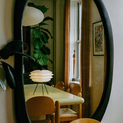 Dining room with round mirror reflecting a table and chairs, plant, and window.