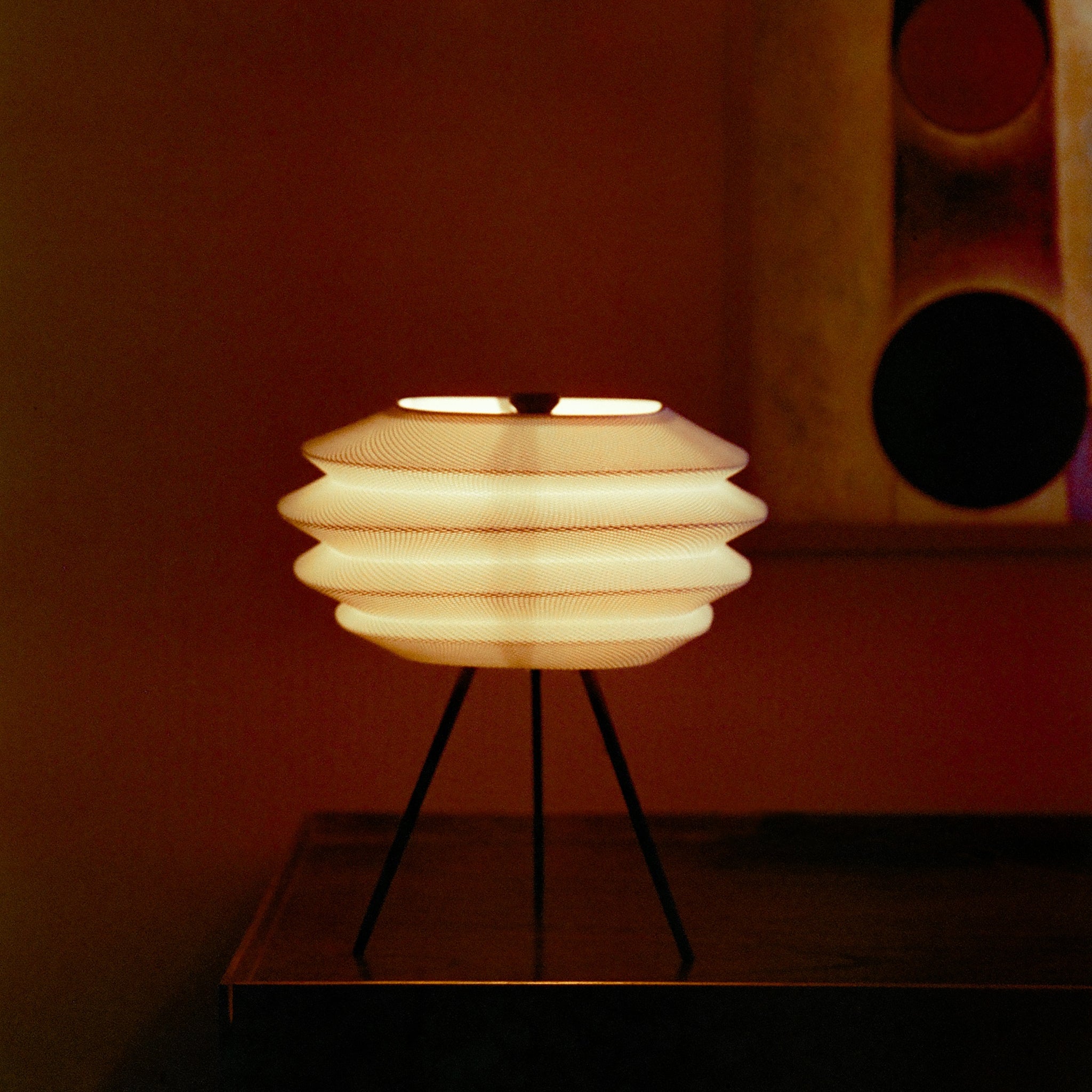 Decorative lamp with a ribbed design on a stand against a dark background
