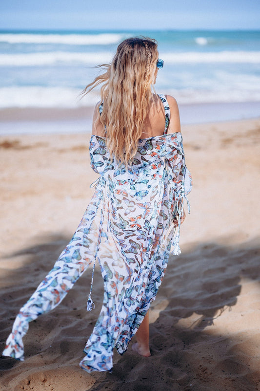 Woman in a floral dress walking on a beach with ocean waves in the background