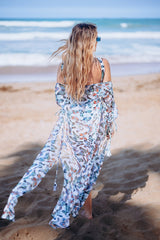 Woman in a floral dress walking on a beach with ocean waves in the background