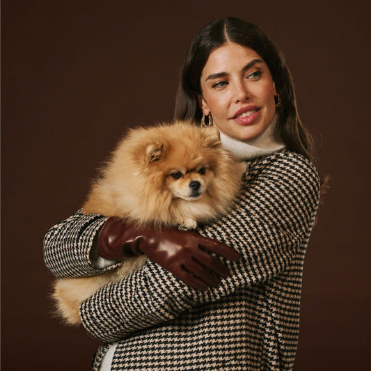 Woman wearing brown leather gloves while holding a fluffy dog against a brown background