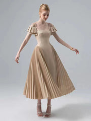 Woman wearing a beige dress with ruffled sleeves on a plain background