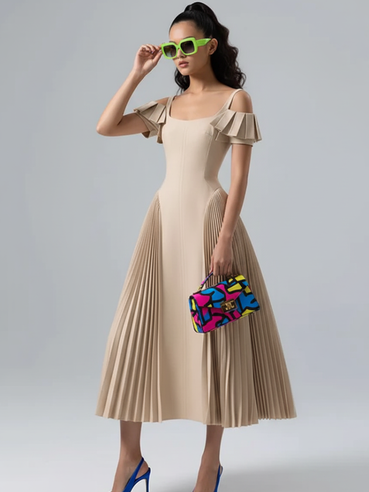 Woman wearing a beige pleated dress with colorful clutch and sunglasses on a gray background