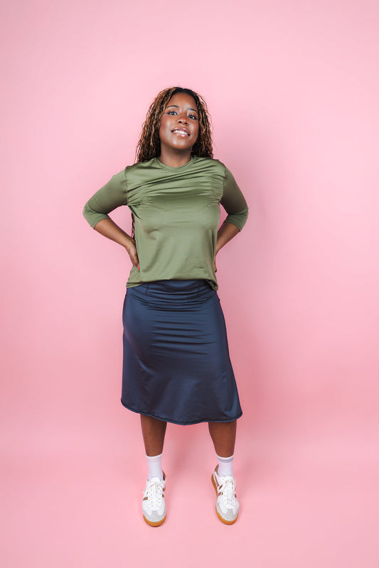 Woman wearing a green top and navy skirt on a pink background