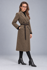 A woman modeling a brown and beige houndstooth double-breasted coat with a matching belt, styled with a black turtleneck, black tights, and black ankle boots against a gray studio background.