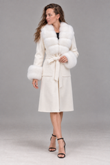 A woman models a white faux fur coat with a matching tie belt, styled with black strappy high-heeled sandals against a neutral gray studio background.