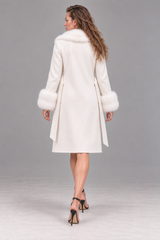A woman shown from the back wearing a long cream-colored coat with fluffy fur trim at the collar and cuffs, paired with black high-heeled sandals, against a neutral gray studio background.