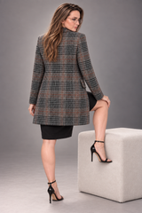A woman wearing a black, brown, and beige plaid blazer over a black dress, posing next to a light gray cube on a gray studio background.