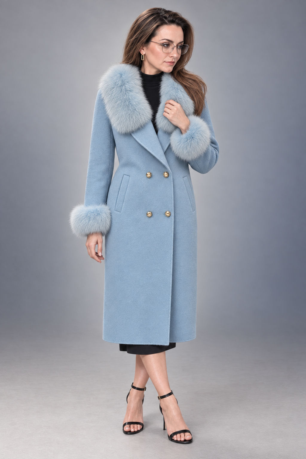 A woman models a light blue double-breasted coat with a fluffy light gray faux fur collar and cuffs, styled with a black top, black skirt, and black high-heeled sandals against a gray studio background.