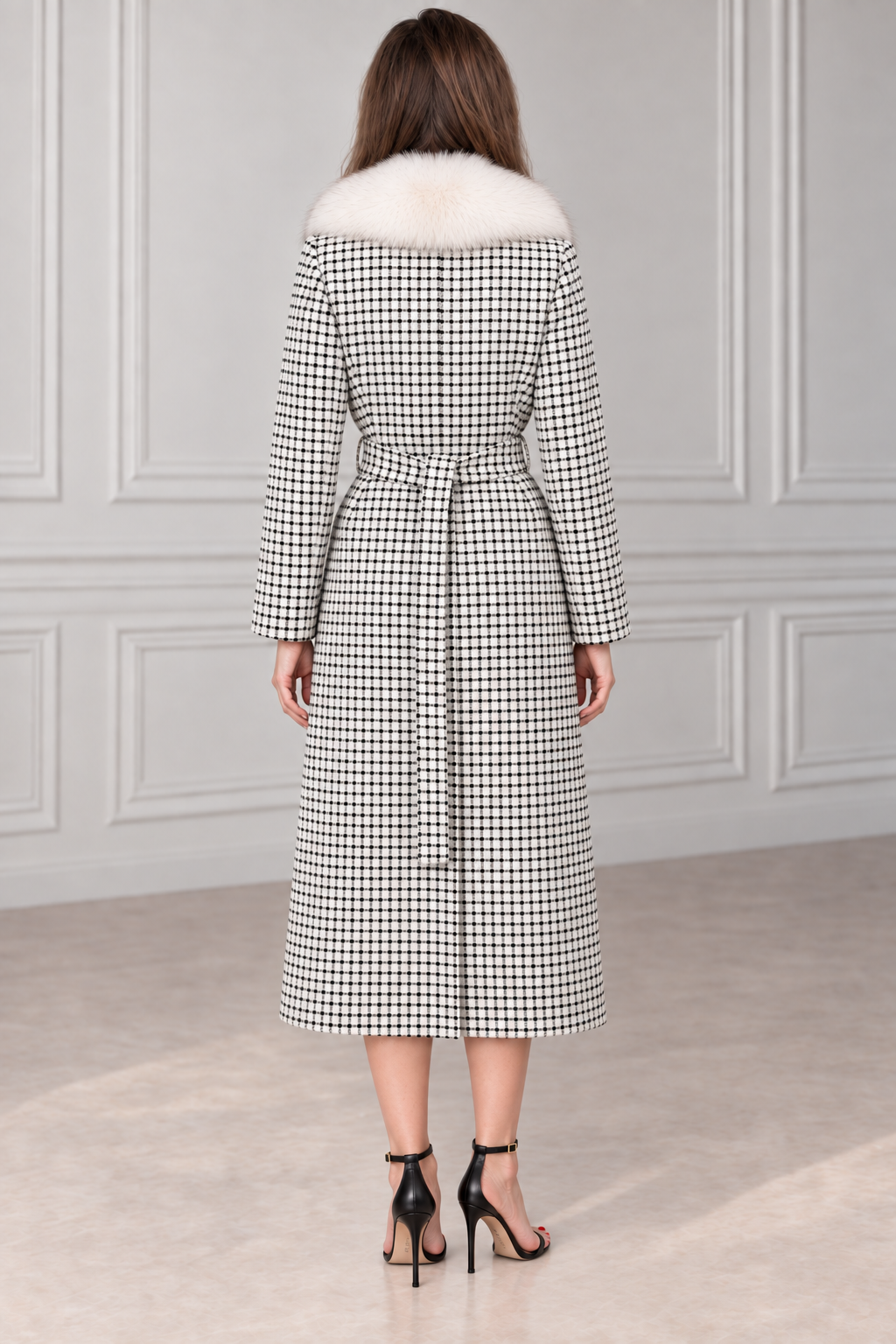 A woman viewed from the back wearing a long black and white houndstooth coat with a white fur collar and a matching waist tie, paired with black high-heeled sandals.